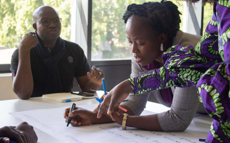 Women leaning over a table to write on their flipchart during an iCRA training.