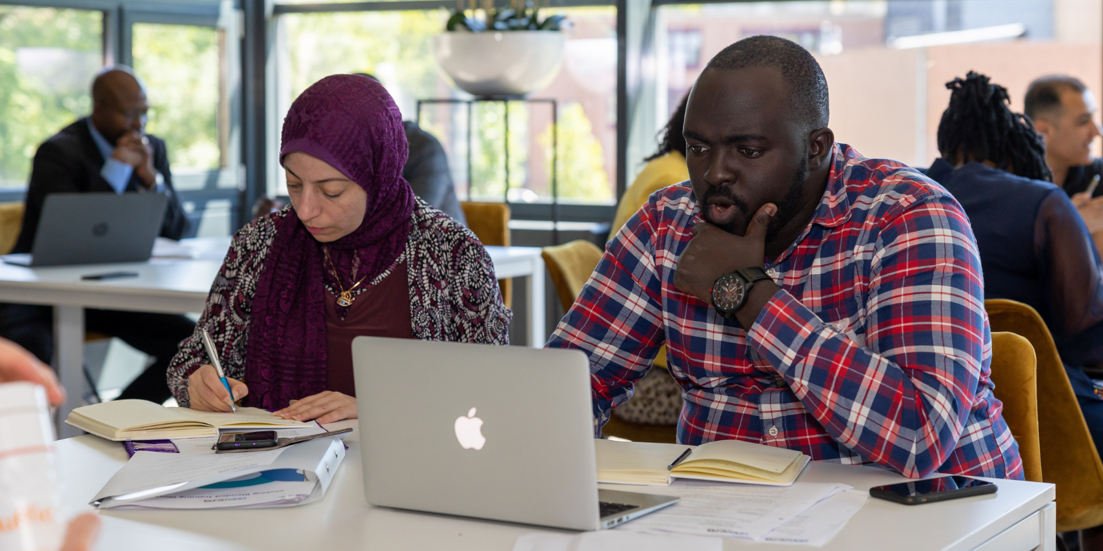 Man looking suprised at his laptop screen whilst the woman next to him writes in her notebook